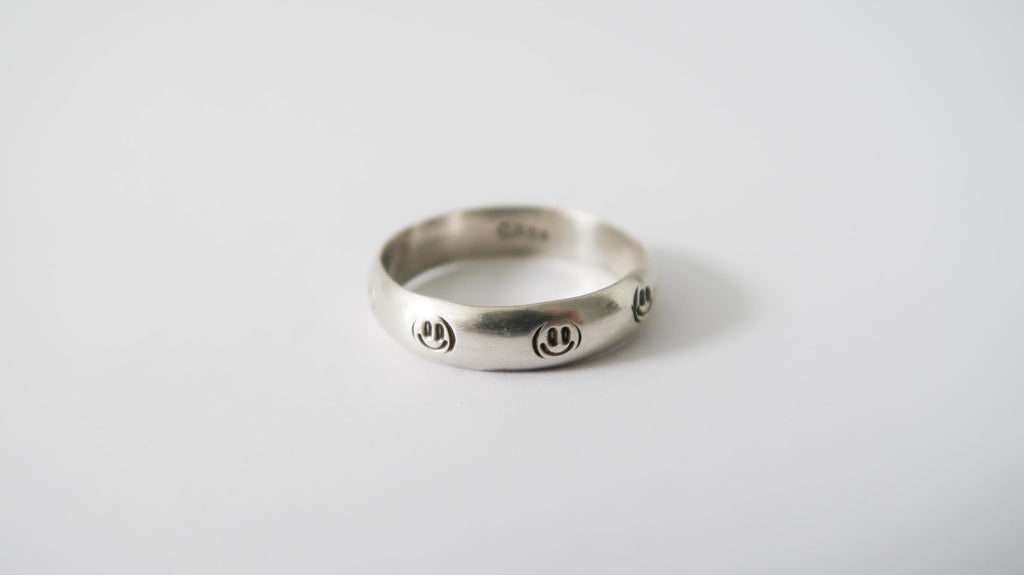 Silver ring with engraved smiley faces on a light background