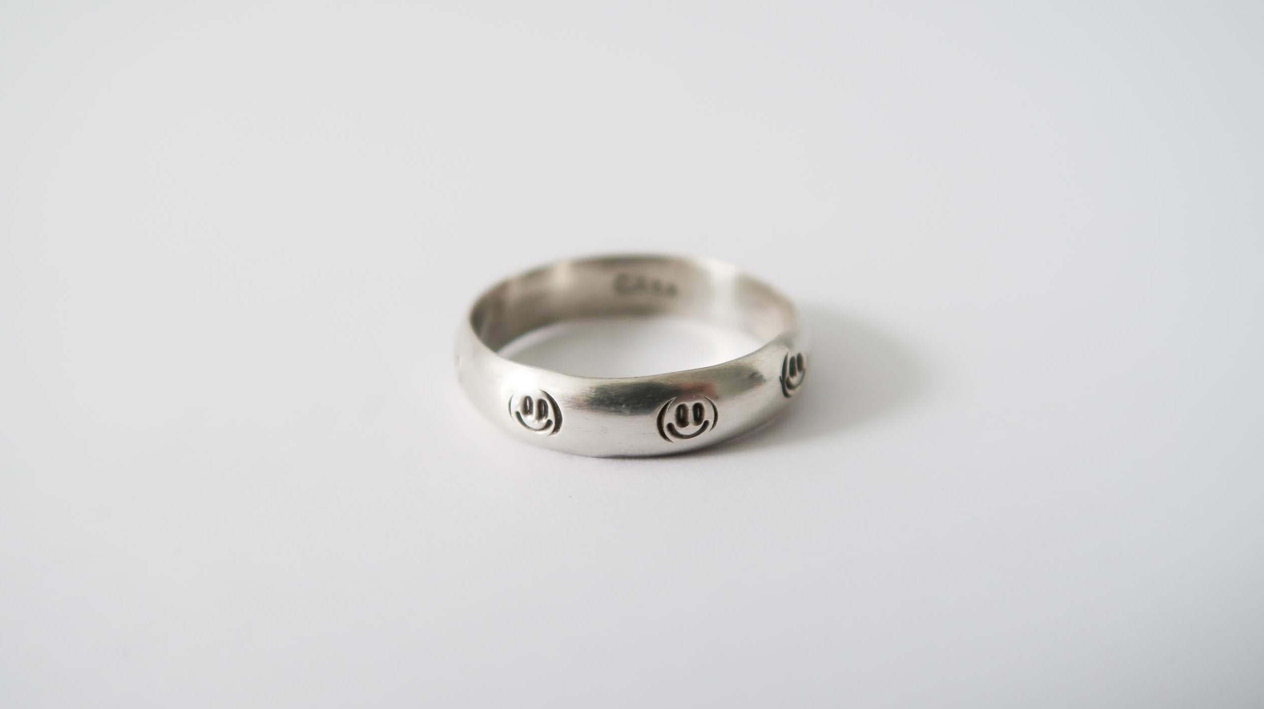 Silver ring with engraved smiley faces on a light background